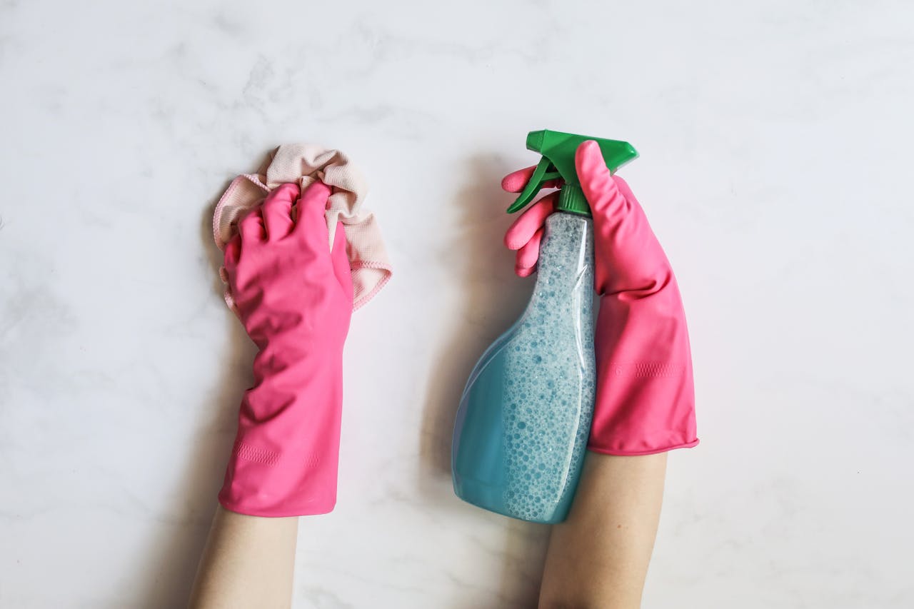 home-services-01 A pair of hands in pink gloves are cleaning with a spray bottle on a white background.